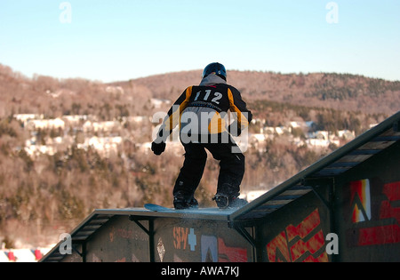 A young male snowboarder performs a freestyle stunt by sliding down or riding a railing Stock Photo