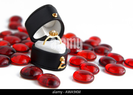 Photo of a heart shaped black box with engagement ring made of gold and with a pearl on the top, surrounded by little red glass stones. Stock Photo