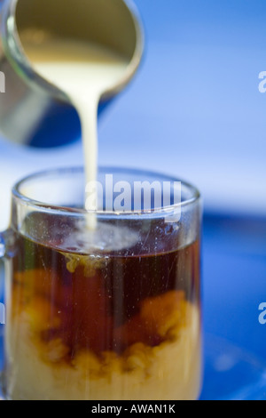 Sequence of pouring milk from a stainless steel jug into a glass of tea against blue background Stock Photo