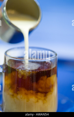 Sequence of pouring milk from a stainless steel jug into a glass of tea against blue background Stock Photo