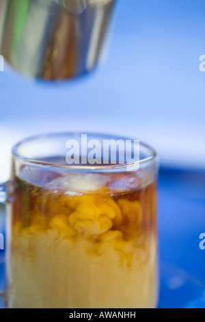 Sequence of pouring milk from a stainless steel jug into a glass of tea against blue background Stock Photo