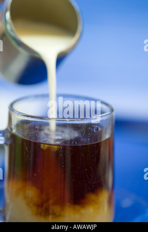 Sequence of pouring milk from a stainless steel jug into a glass of tea against blue background Stock Photo