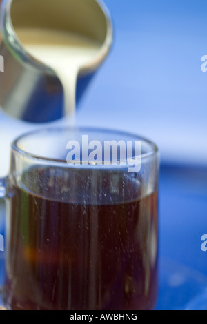 Sequence of pouring milk from a stainless steel jug into a glass of tea against blue background Stock Photo