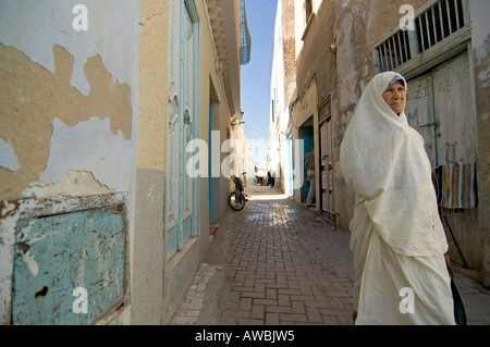 Typical street in the Arab world, an old woman in her traditional white dress, photo taken in Kairouan, Tunisia. Stock Photo