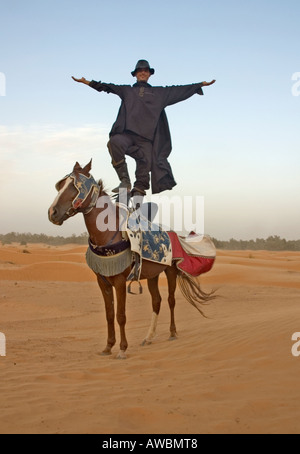 A tour guide dressed as Zorro stands on his horse with arms outstretched in Sahara desert near the oasis Ksar Ghilane, Tunisia Stock Photo