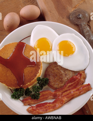 fast food hearty breakfast 2 two eggs sunny side  bacon strips sausage stack of pancakes syrup brown eggs parsley garnish Stock Photo