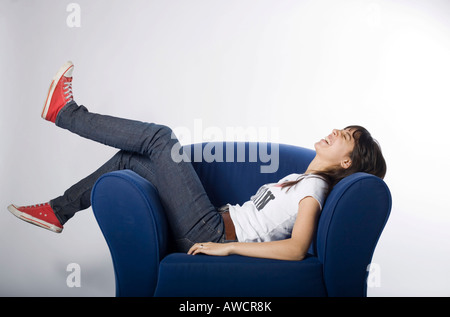 Young woman comfortably lying on a blue armchair Stock Photo
