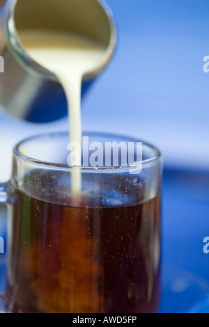 Sequence of pouring milk from a stainless steel jug into a glass of tea against blue background Stock Photo