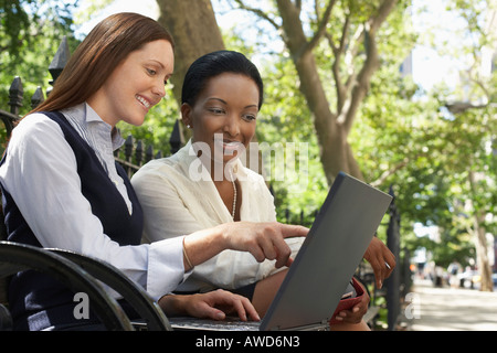 Two female colleagues using laptop on park bench Stock Photo