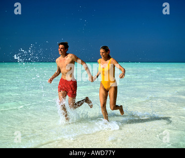 Young couple jogging through shallow water, Maldives, Indian Ocean Stock Photo