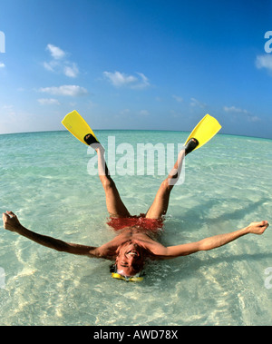 Young man wearing flippers laying in shallow water, vacation, Maldives, Indian Ocean Stock Photo