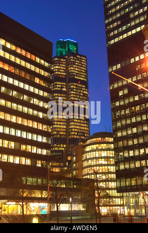 Tower 42 in the city of London, lit up at Nightime, sandwiched between other buildings Stock Photo