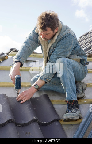 a builder fitting tiles to a roof of a new home Stock Photo