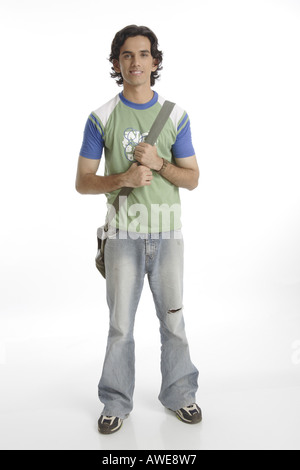 Teenage boy holding strap of back bag smiling wearing torn faded blue jeans and top green tee shirt long hair walking shoes Stock Photo
