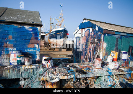 Boat repairers paint outdoor building shed, test colour daubs, brush marks, and paint tins at Banff fishing boat repair yard North East Scotland UK Stock Photo