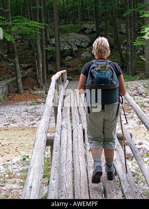 hiker woman hiking on a foothpath over a wooden bridge in a forest Stock Photo