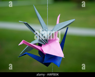Blue pink and grey origami swans hanging from a string in front of a blurred backgound of green grass on the University of Puget Stock Photo