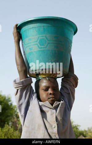 Boy carrying a pail of water on his head, Sahel region, Cameroon, Africa Stock Photo