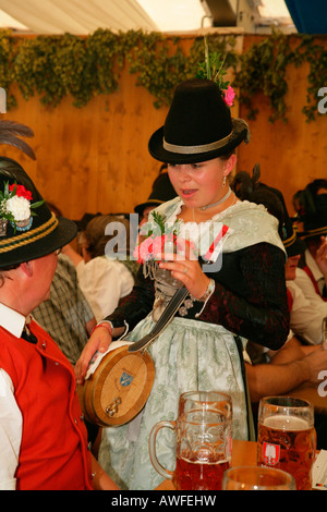 Young woman dressed in national costume holding a bottle of schnapps in a beer tent at a folk festival in Muehldorf am Inn, Upp Stock Photo