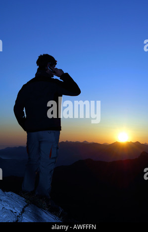 Man with mobile phone at sunrise on a mountain top, Breitenstein Mountain, Bavarian foothills, Wendelstein Group, Upper Bavaria Stock Photo