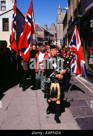 dh Norwegian Constitution Day KIRKWALL ORKNEY Bagpiper leading street parade Albert street Flags procession piper scottish national dress Stock Photo
