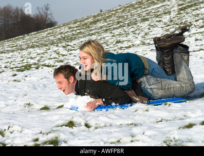 man with woman on his back lying on a sledge, sleigh, going down a hill, husband wife, having fun Stock Photo