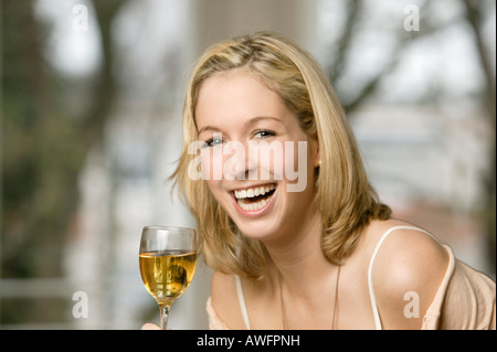 Young blonde woman drinking a glass of white wine, laughing Stock Photo