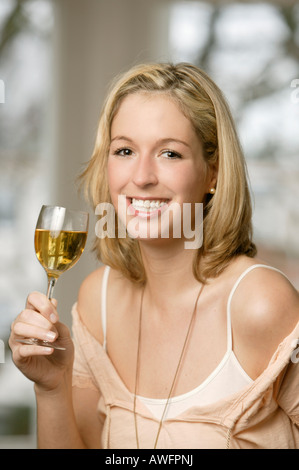 Young blonde woman drinking a glass of white wine, laughing Stock Photo