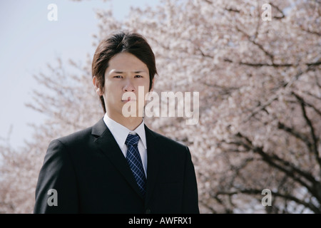 A young man in suit standing in front of cherry blossoms Stock Photo
