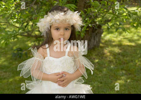 Little girl aged 3 in a bridesmaid dress beneath a tree on a green grass lawn Stock Photo