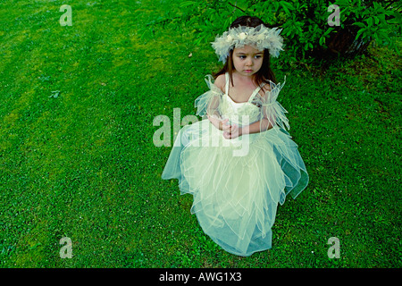 Little girl aged 3 in a bridesmaid dress beneath a tree on a green grass lawn Stock Photo