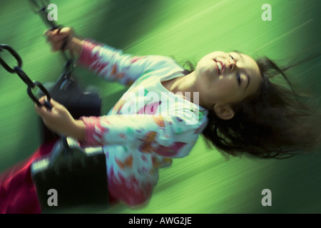 Pretty little girl three years old in blurred motion on a swing at an adventure playground Stock Photo