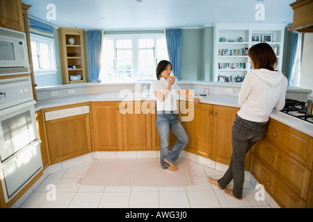 Two young women talking in kitchen Stock Photo