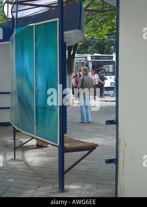 Bus stop with advertising panels and bus shelter with canopy, wooden seating, passengers waiting, single decker bus front, Gomel, Belarus Stock Photo