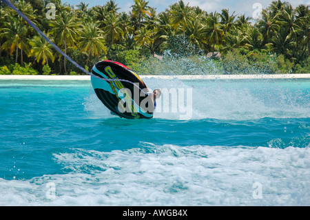 Horizontal close up of a young man about to fall off an inflatable donut whilst tubing in the sea on a bright sunny day. Stock Photo