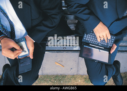 Two business men sitting on a bench using a palm and laptop having lunch Stock Photo
