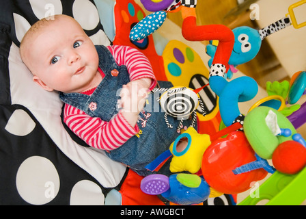 Horizontal portrait of a cute Caucasian baby girl lying on a colourful baby playgym mat to stimulate and develop her senses. Stock Photo