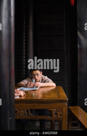 A boy sitting at a desk texting on his mobile. Pingyao, People's Republic of China Stock Photo