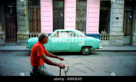 Old man cycling past a classic American car in Havana Cuba Stock Photo