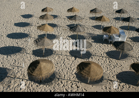 Thatched umbrellas make pools of shade on the beach named Praia da Rainha in the city of Cascais Portugal. Stock Photo