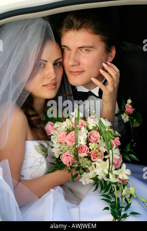 Beautiful smiling bride in white dress on wedding day. She is getting out of a wedding car limousine with her husband Stock Photo