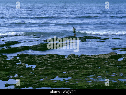 Person fishing on rock near breaking waves Stock Photo