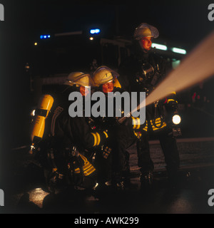 Two firemen spraying water on fire with hose Stock Photo