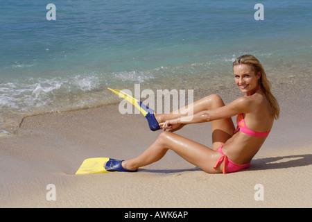 woman in pink bikini sat on a beach putting on yellow fins Stock Photo