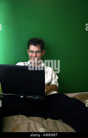 A man using a laptop computer next to a green wall.  As he smiles you have to wonder what he is looking at. Stock Photo