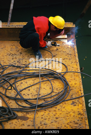Welder squatting, wearing protective mask and yellow hardhat on contruction site Stock Photo