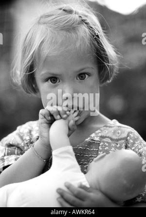 Little girl holding baby doll, portrait, b&w Stock Photo