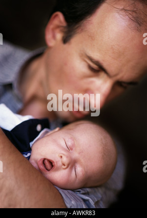 Man holding and looking down at sleeping baby, focus on baby, eyes closed and mouth open, close-up Stock Photo