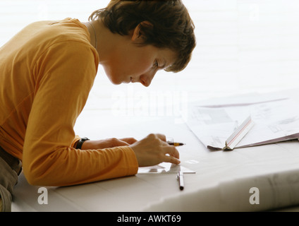 Woman bending over table, holding set square and pen, side view Stock Photo