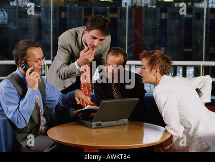 Three men and a woman sitting at table, looking at laptop computer Stock Photo